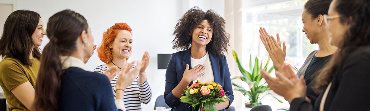 A woman with a bouquet of flowers receives applause from colleagues